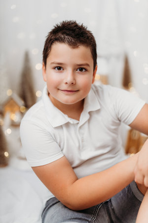 Studio portrait of a 10-year-old boy in a festive Christmas setting. Surrounded by warm lights and holiday decorations, he exudes childhood joy and wonder, capturing the magic of the season.の写真素材