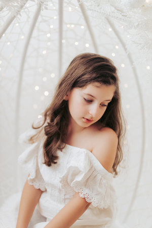 Studio portrait of a delicate 10-year-old girl in a festive Christmas setting. Surrounded by warm lights and holiday decorations, she exudes innocence and joy, capturing the magic of the season.の写真素材