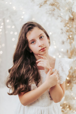 Studio portrait of a delicate 10-year-old girl in a festive Christmas setting. Surrounded by warm lights and holiday decorations, she exudes innocence and joy, capturing the magic of the season.の写真素材