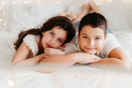 Studio portrait of preteen siblings or cousins in a festive Christmas setting. Surrounded by warm lights and holiday decorations, they share joyful moments, capturing the magic and warmth of the season.の写真素材