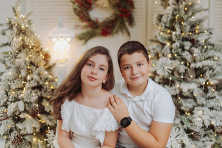 Studio portrait of preteen siblings or cousins in a festive Christmas setting. Surrounded by warm lights and holiday decorations, they share joyful moments, capturing the magic and warmth of the season.の写真素材