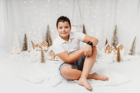 Studio portrait of a 10-year-old boy in a festive Christmas setting. Surrounded by warm lights and holiday decorations, he exudes childhood joy and wonder, capturing the magic of the season.の写真素材