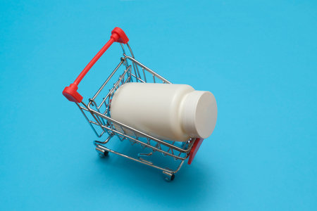 metal shoppin cart with pills plastic bottle on blue background