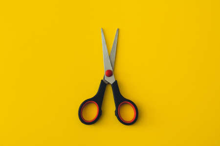Minimalist photo of black scissors on yellow background. Flat lay shot of opened black scissors with central composition.の写真素材