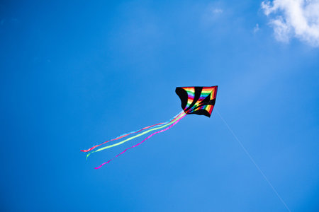 A colorful kite flying in the blue sky, concept of freedom, concept of summer. Rainbow kite flying in the wind.の写真素材