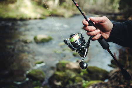 Male hands holding fishing rod or angler over fast forest river.の写真素材