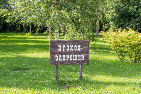 A rustic wooden sign stands in a vibrant green park, conveying a warning about restricted access. Surrounding trees and plants complement the outdoor setting, creating a serene atmosphere.の写真素材