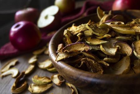 Homemade dried apples in a bowl and fresh ripe apples on wooden tableの写真素材