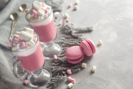Pink hot chocolate winter drink with whipped cream and marshmallows. Macaroons and spoons. Copy...