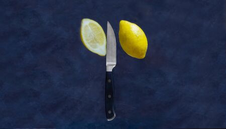 The sliced Yellow lemon and A kitchen knife are floating in the air, with the image stopped moving on dark blue background. Minimalism conceptの写真素材