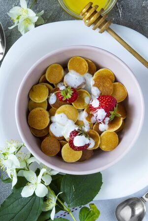 Trendy food - pancake cereal. Heap of mini cereal pancakes with strawberries and yogurt in light boul. Top view or flat lay.の写真素材