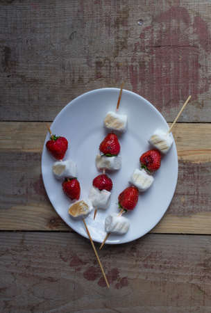 Gourmet Grilled Strawberry and Marshmallow on Stick on wooden skewers in white plate on rustic wooden backgroundの写真素材