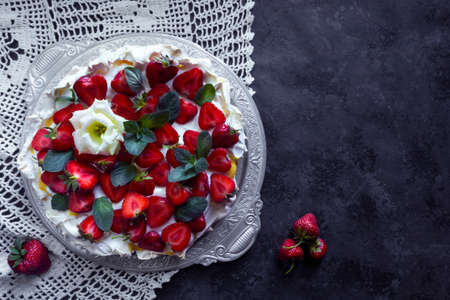 Homemade meringue cake Anna Pavlova with straeberries and mint on the knitted tablecloth. Copy space on dark backgroundの写真素材