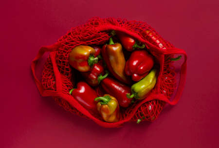 Fresh bell peppers in eco friendly bag on the red background.の写真素材