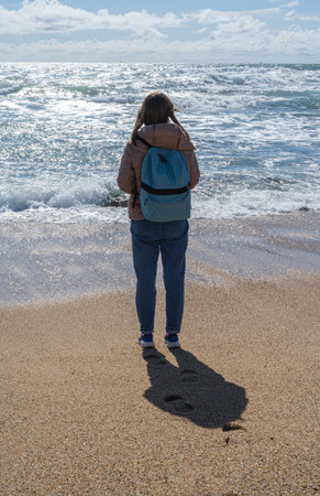 back view of woman with backpack standing on the ocean beach