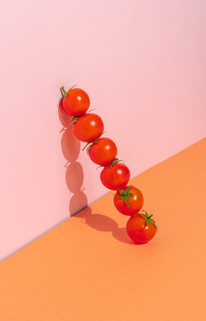 Fresh cherry tomatoes in a row on a pink and orange background.の写真素材