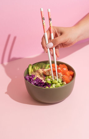 Hands eating poke bowl with salmon on pink background