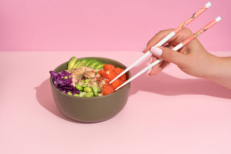 Hands eating poke bowl with salmon on pink background