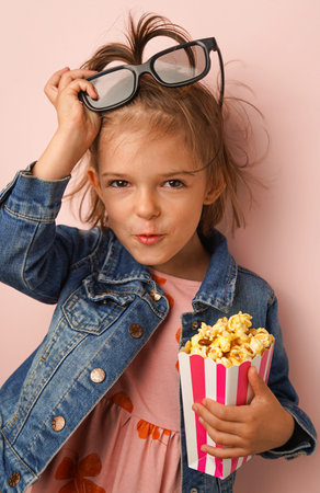The 3 years old girl with sweet popcorn and cinema glasses