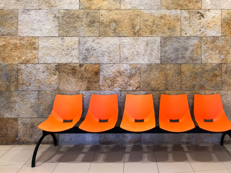 Orange benches in a waiting room with a stone wall Social distance. Copyspace. Waiting room with bright colors.の写真素材