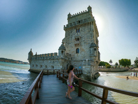 White Caucasian woman observing the Belem Tower in Lisbon on a dramatic back-lit sunset. Surrounded by waterのeditorial素材