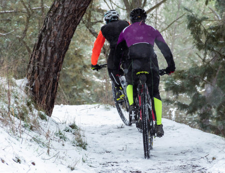 Btt cyclists get out of focus in the snow. Extreme mtb in the snow with the road frozen in the middle of a forest while it snows. Snowy image. Concept of extreme sport in winterの写真素材
