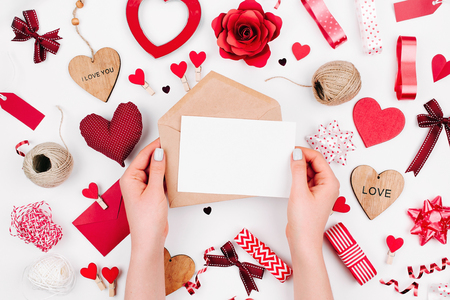 Female hands are holding a Blank white greeting card on white background with romantic decoration. flat layの写真素材