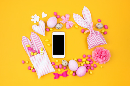 Smartphone mock up with frame of Easter eggs,  bunny gift bags with candies and decoration.  Flat layの写真素材