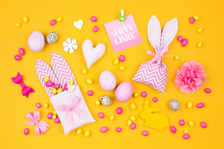 Easter holiday concept with pink and yellow Easter eggs, fabric bunny gift bags with candies and decorationの写真素材