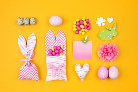 Flat lay stylish set: pink and yellow Easter eggs, fabric bunny gift bags with candies and decorationの写真素材