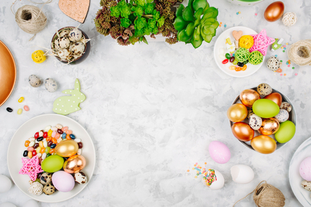 Workspace with easter decoration. Painted eggs in trays, candy, flowers with copy space. Holiday background. Flat lay, top viewの写真素材
