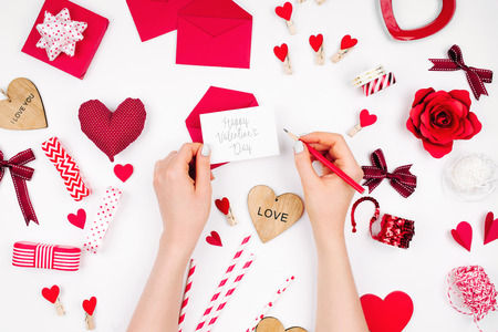 Women's hands holding valentine card on white background with romantic decoration. flat layoutの写真素材