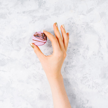 Female hand holding lavender macaroon decorated with chocolate on a gray background.  Minimalismの写真素材