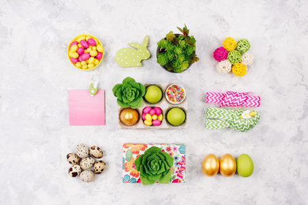 Flat lay stylish set: pink, yellow and green Easter decorations, eggs, candy and succulents in paper...