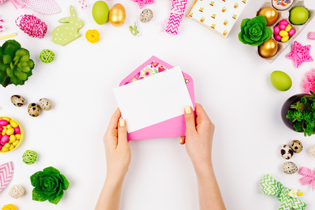 Woman holding a empty card and pink envelope. Beautiful spring mock up. Easter concept. Flat lay, top viewの写真素材