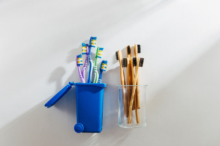 Eco friendly bamboo toothbrushes in glass and plastic toothbrushes in trash bin. Zero waste, plastic free, ecology concept.の写真素材
