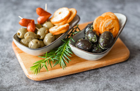 Olives, delicious Italian appetizer, green and black olives with herbs in olive oil on the wooden cutting boardの写真素材