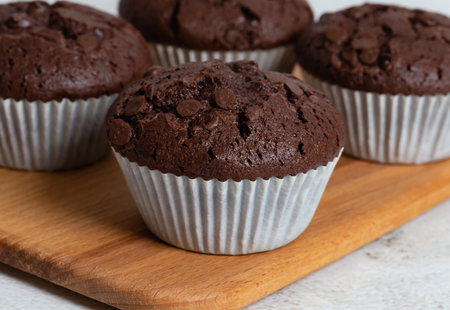 Plain chocolate muffins with chocolate chips in white paper cups, close-up view.の写真素材