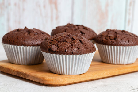 Plain chocolate muffins with chocolate chips in white paper cups, close-up view.の写真素材