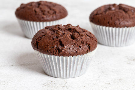 Plain chocolate muffins with chocolate chips in white paper cups, close-up view.の写真素材