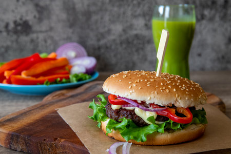 Freshly made burger on the cutting board on the wooden table and a green smoothie in the backgroundの写真素材