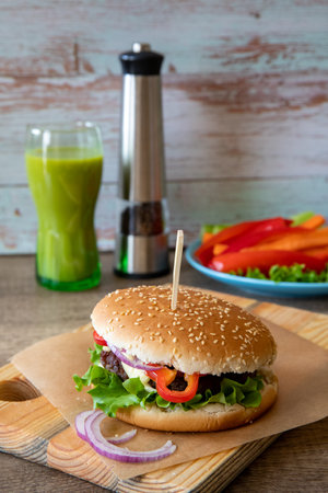 Freshly made burger on the cutting board on the wooden table and a green smoothie in the background, with copy space, verticalの写真素材