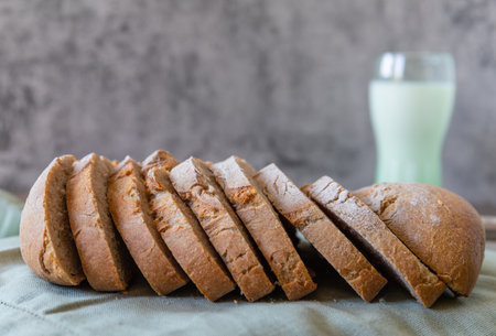 Rye bread sliced on the light green textile, close up. In the background a glass of milk out of focus, copy spaceの写真素材
