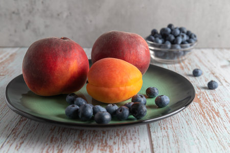 Several peaches, an apricot and several ripe blueberries standing on a plate on the table, close-up, vertical, food and drink, concrete backgroundの写真素材