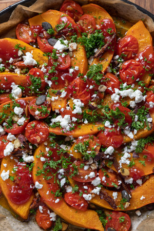 Delicious Hokkaido pumpkin with curry, mini tomatoes, hazelnuts, pumpkin seeds, dates and sheep's cheese baked on a dark rustic background, top view, verticalの写真素材