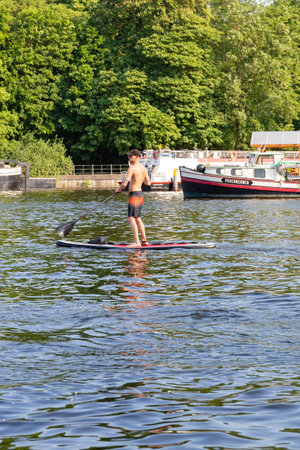 Berlin-Treptow, Germany - June 9, 2023, Young man paddling on a stand-up paddleboard on the River Spree. Summer activities and water sports. Space to copy. selective focus.のeditorial素材