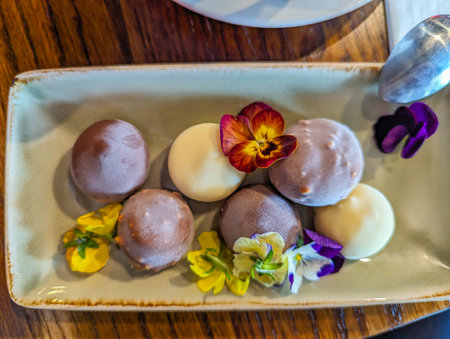 A delightful presentation of mochi paired with coffee, adorned with edible flowers on a ceramic plate, showcasing an elegant dining experience in a cozy cafe setting.の写真素材