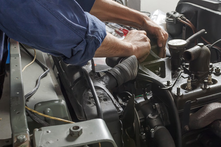 Auto mechanic working under the hood of an old car engine.の写真素材