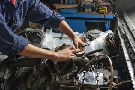 Auto mechanic working under the hood of an old car engine.の写真素材
