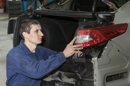 Young mechanic installs tail light on the vehicle.の写真素材